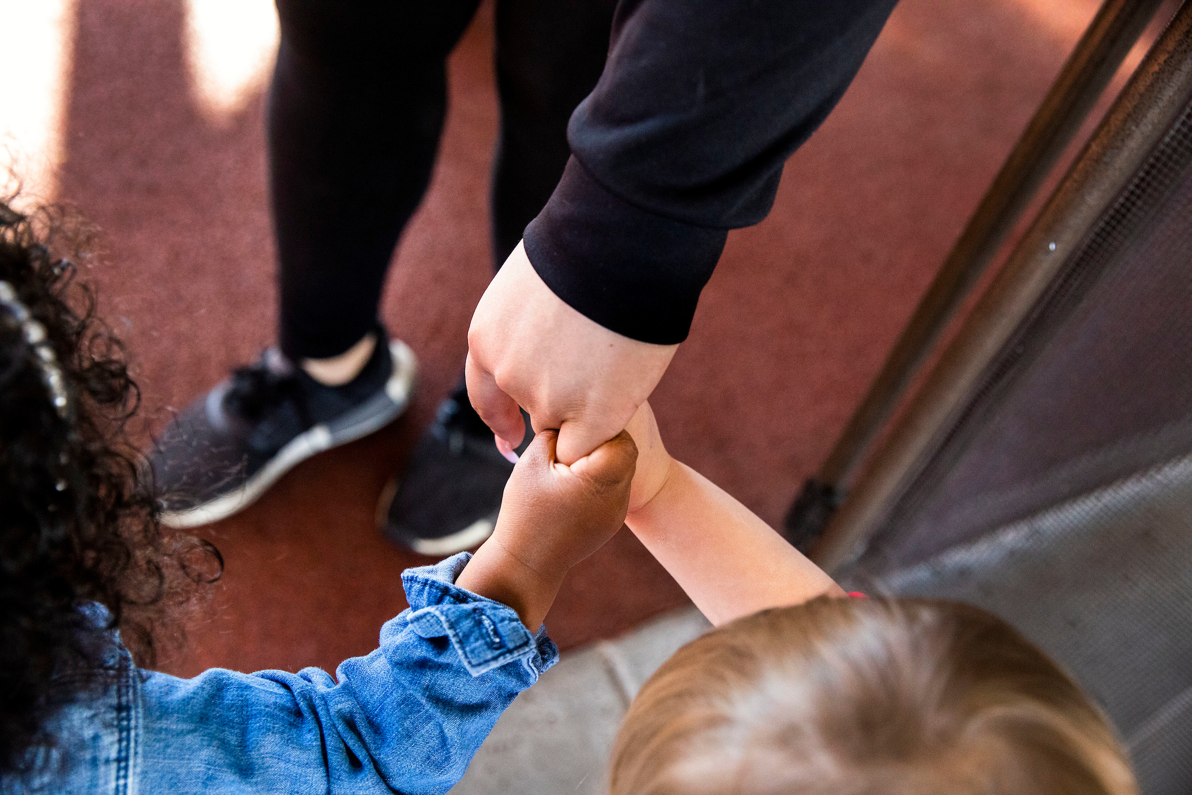 Close=up shot of two preschool children holding a teacher's hand